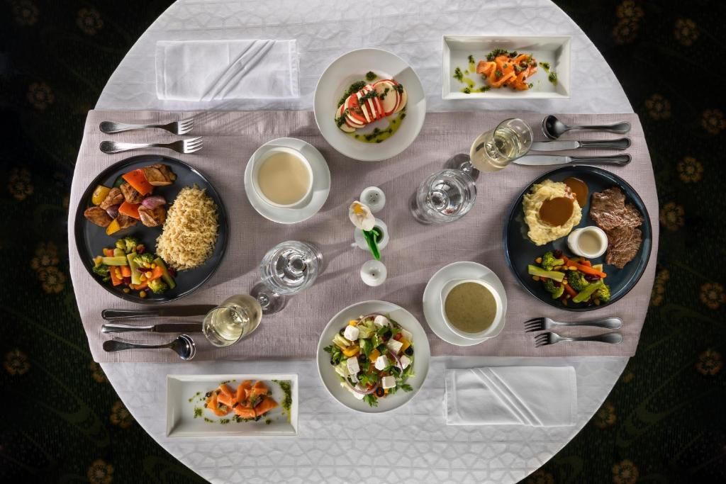 A round dining table with various dishes and drinks, surrounded by white napkins and cutlery.
