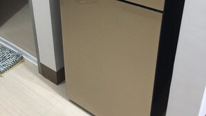 Un refrigerador de dos puertas con un logotipo en la puerta superior, ubicado en una cocina con piso de baldosas y pared blanca.