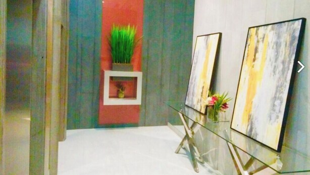 Un pasillo con una mesa de vidrio que exhibe dos cuadros, un panel vertical rojo y una planta verde.