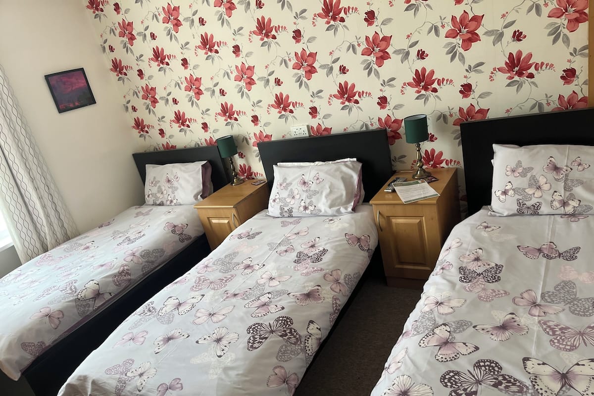 A hotel room with two single beds, a wooden nightstand, a desk, and a floral wallpaper.