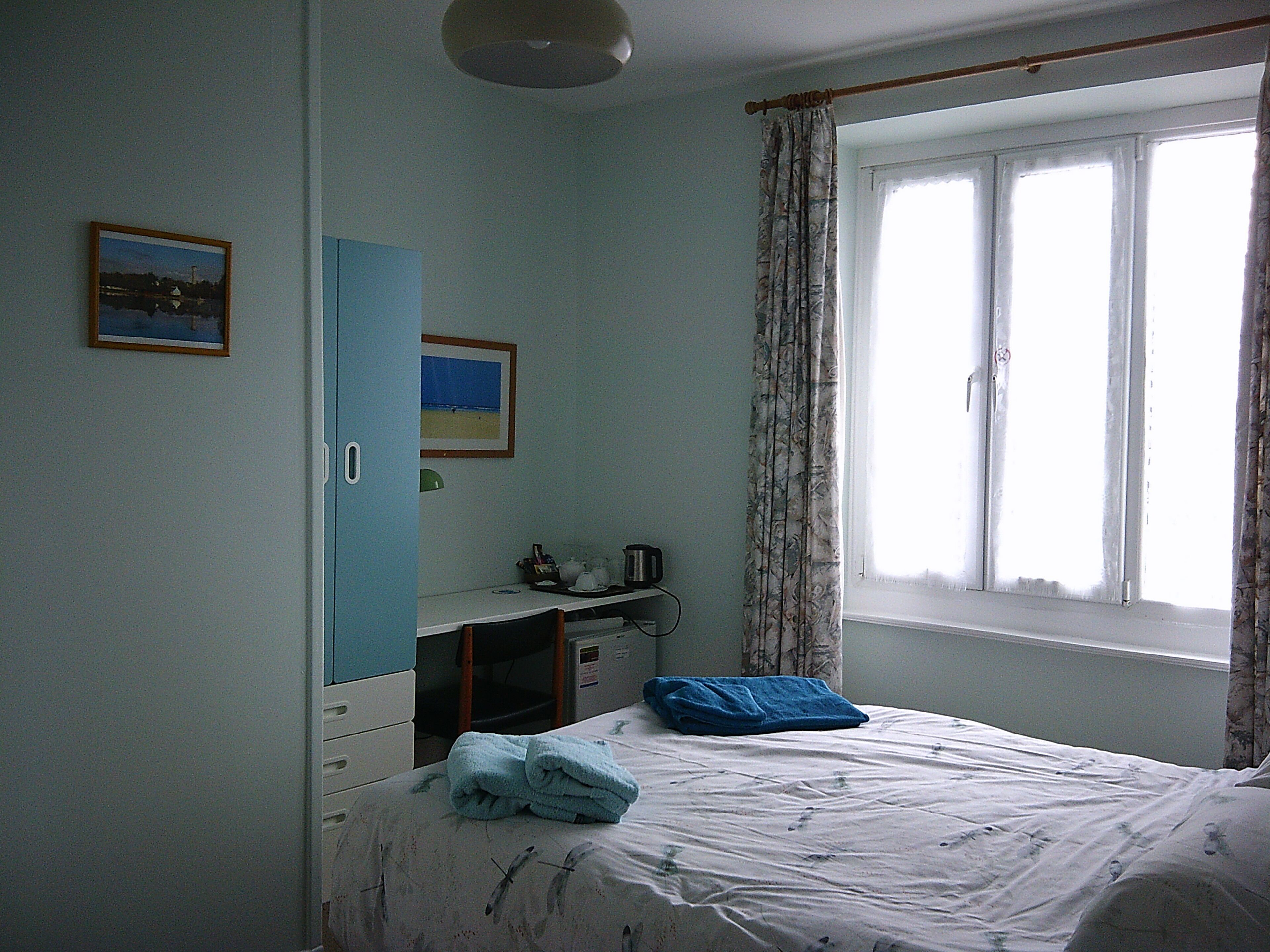 A bedroom with a bed, a desk, a chair, a wardrobe, and a window with curtains.