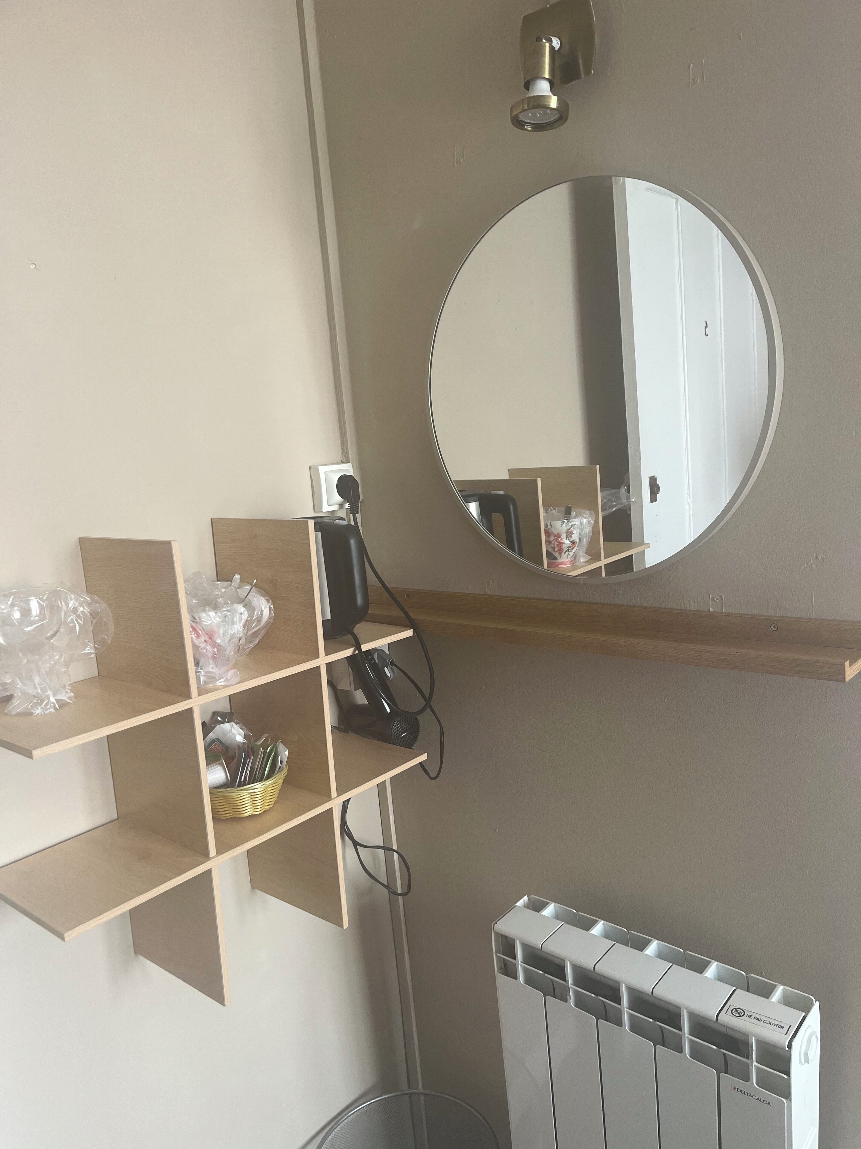 A room with a wooden shelf, a round mirror, a radiator, and a basket on the floor.