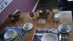 A breakfast table set with plates, cups, cutlery, a bowl of bread, and a glass of juice. - Webb's of Glomel (Glomel)