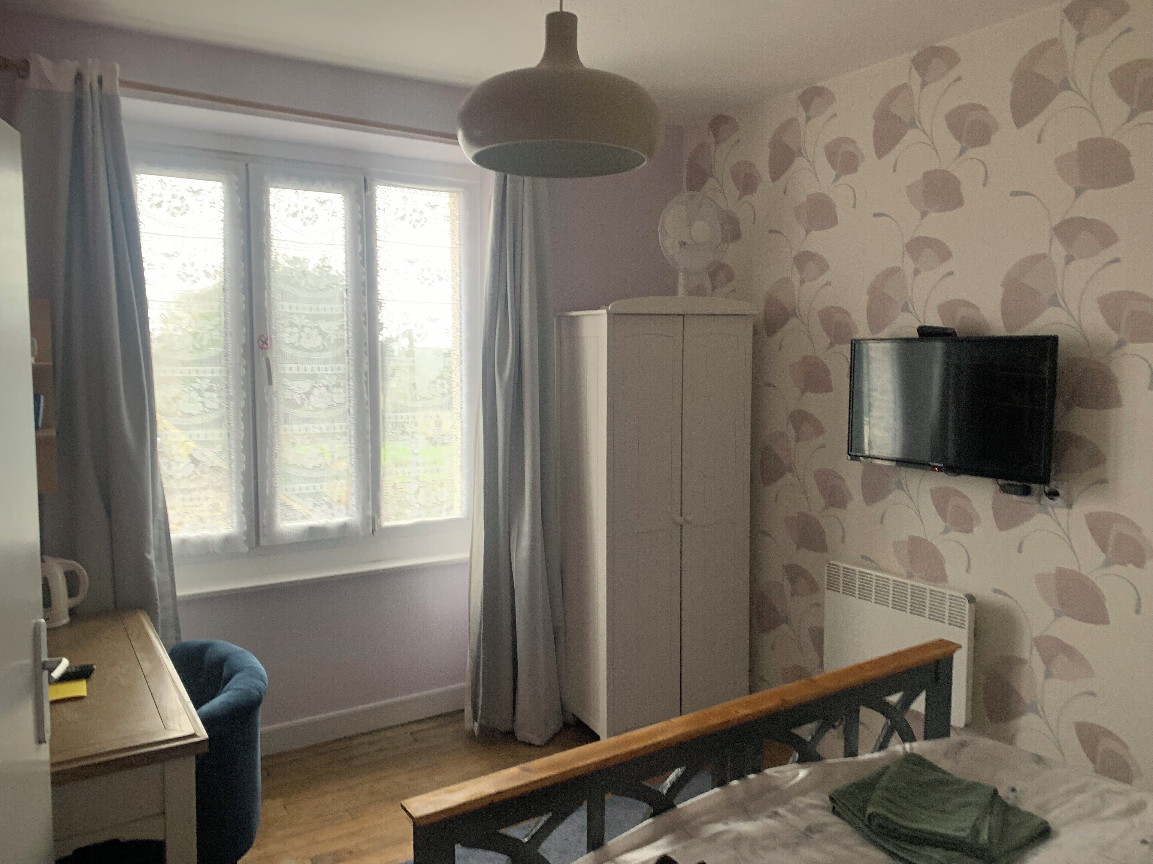 A room with a bed, a desk, a wardrobe, a television, and a window with curtains.