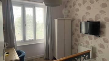 Quarto com cama, escrivaninha, guarda-roupa, televisão e janela com cortinas.
