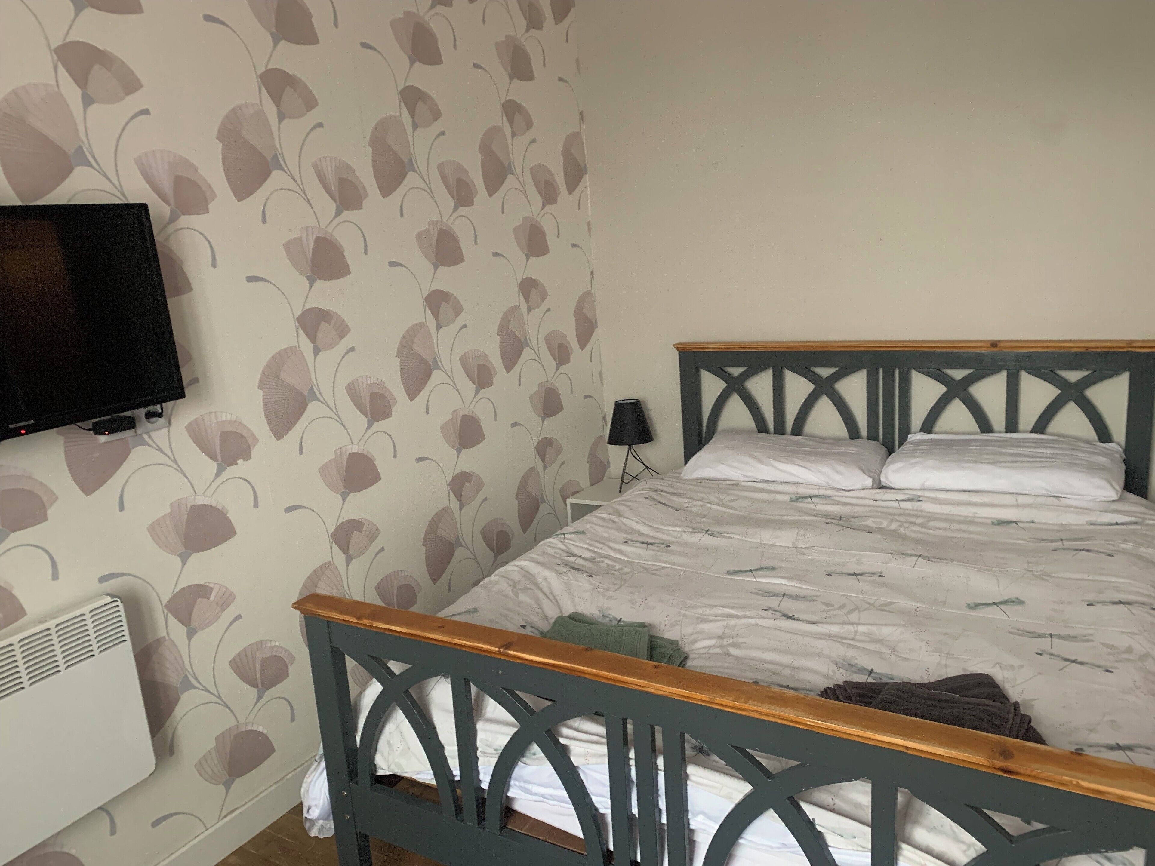 Un dormitorio con una cama, un televisor en la pared y un radiador.