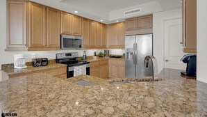 A modern kitchen with granite countertops, stainless steel appliances, wooden cabinets, and a built-in oven. - Island Vacation Condo w/ Breathtaking Views At Waterside! First-Class Amenities! (Fort Myers Beach)