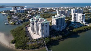 An aerial view of a coastal hotel area with multiple high-rise buildings, a marina, and a bridge connecting the buildings to the mainland. - Island Vacation Condo w/ Breathtaking Views At Waterside! First-Class Amenities! (Fort Myers Beach)