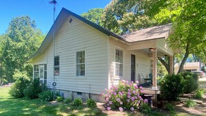 A single-story house with a porch, surrounded by a well-maintained lawn and flowering plants.