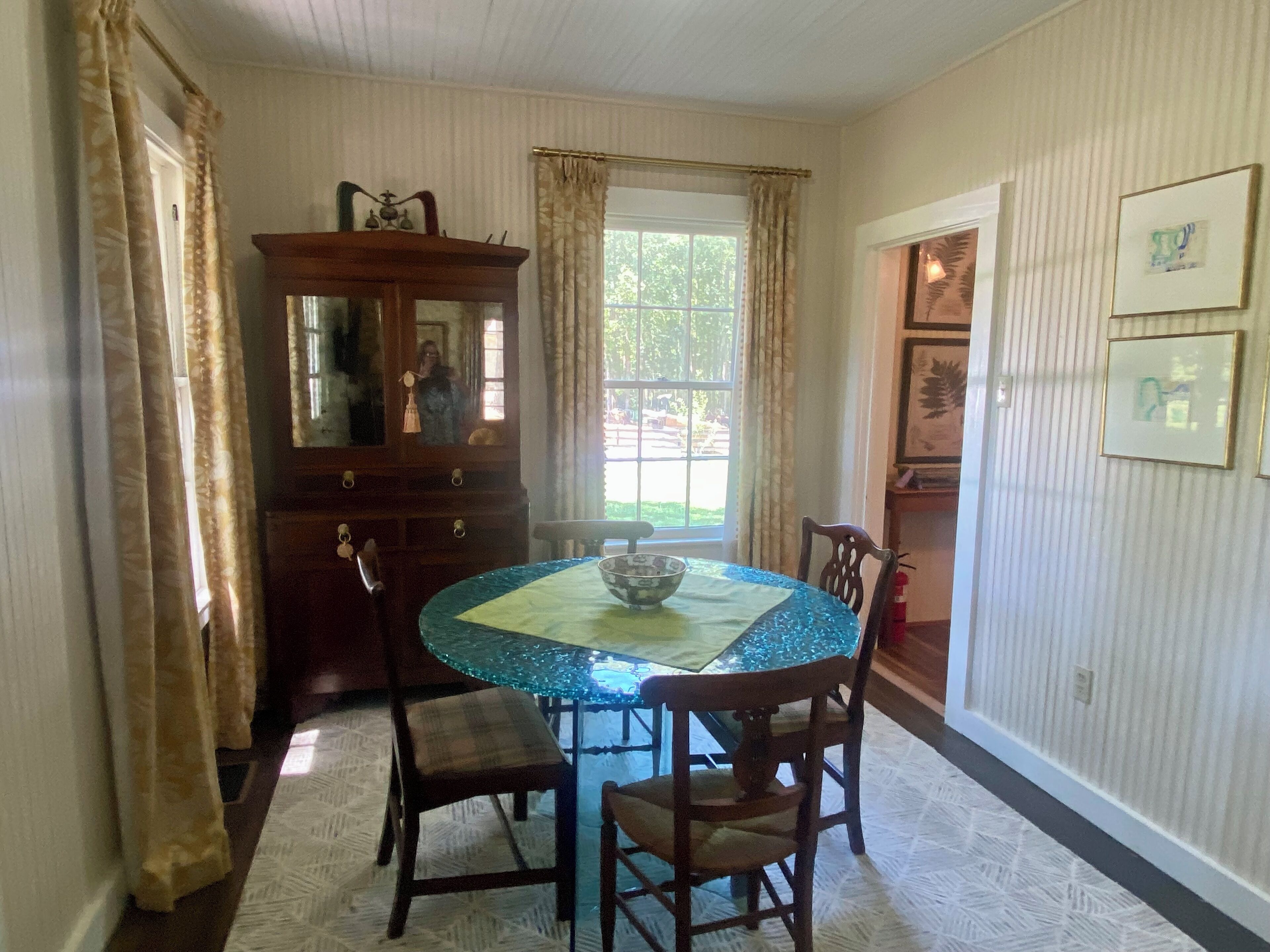 A dining room with a round table, chairs, a wooden cabinet, and a window with curtains.