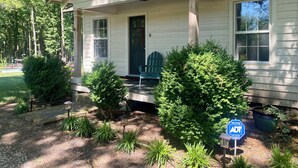A single-story house with a porch, a green chair, and a small garden with various plants.