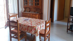 Un comedor con una mesa dispuesta para dos, sillas de madera, un aparador con puertas de vidrio y un televisor sobre un mueble.