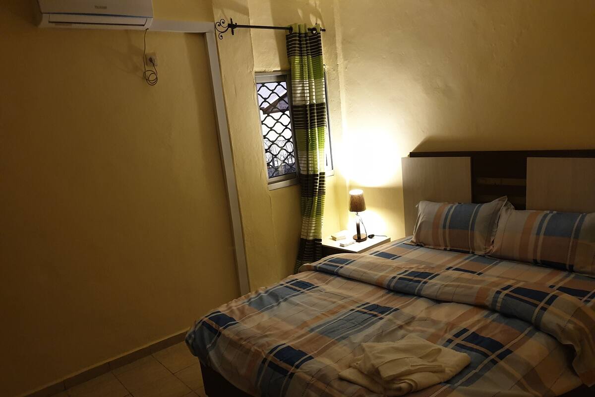 A bedroom with a bed, a nightstand, a lamp, and a window with curtains.