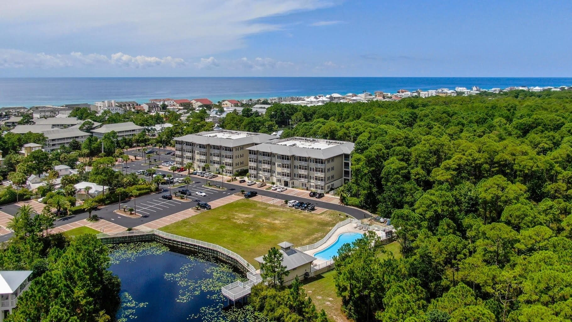 An aerial view of a hotel with a swimming pool, surrounded by dense greenery and a view of the ocean.