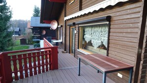 Une cabane en bois dotée d’une terrasse, d’une antenne parabolique et d’une fenêtre avec des rideaux.