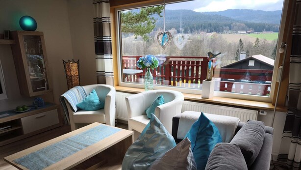 Un salon chaleureux avec un canapé, des fauteuils, une table basse et une grande fenêtre donnant sur un paysage rural.