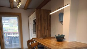 Une cuisine moderne agrémentée d’éléments en bois, un coin repas avec des chaises et une vue à travers une porte vitrée.