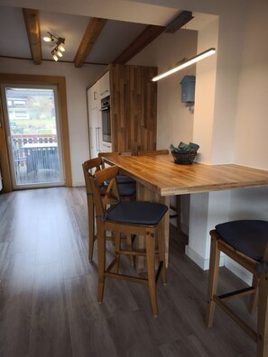 A modern kitchen with wooden accents, a dining area with chairs, and a view through a glass door.