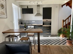 A modern kitchen with a checkered floor, a dining area with a table and chairs, and a staircase leading to another level.
