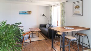 A modern living space with a wooden dining table, bar stools, a sofa, and a large green plant.
