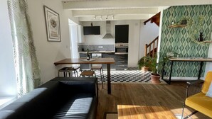 A living room with a black leather sofa, a wooden coffee table, and a yellow chair. There is a kitchen in the background with modern appliances and a checkered floor.