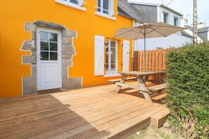 A wooden deck with a picnic table and umbrella, adjacent to a building with a bright orange facade and white shutters.