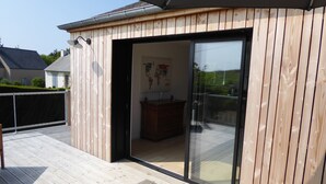 Eine Holzdielen-Terrasse mit einer Schiebetür, die zu einem Innenraum führt, in dem sich ein Holzkasten und eine Karte an der Wand befinden.