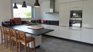 Eine moderne Küche mit einer großen Kochinsel, Holzbarhocker, einem eingebauten Backofen und Pendelleuchten.