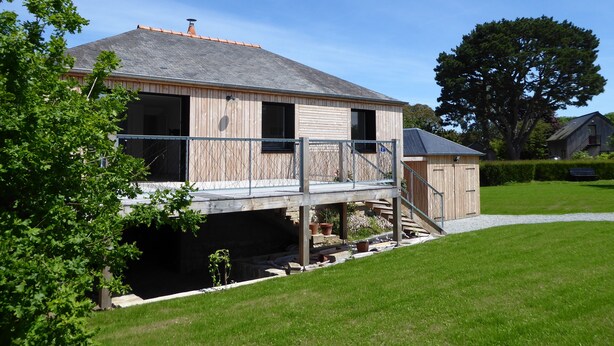 Ein zweigeschossiges Holzhaus mit Balkon, überdachter Veranda und einem kleinen Garten.