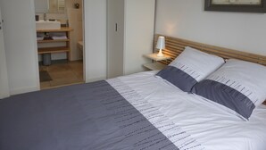 Ein Schlafzimmer mit einem Bett, einem Nachttisch mit Lampe, einem Kleiderschrank und einem durch eine offene Tür einsehbaren Badezimmer.