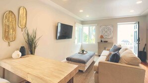 Een moderne woonkamer met een houten eettafel, een bank en een aan de muur bevestigde televisie.