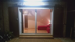 A room with a sliding glass door leading to a bed with red bedding.