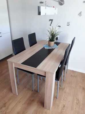 Een eettafel met vier stoelen, een potplant en een wandplank met een klok en enkele spullen.