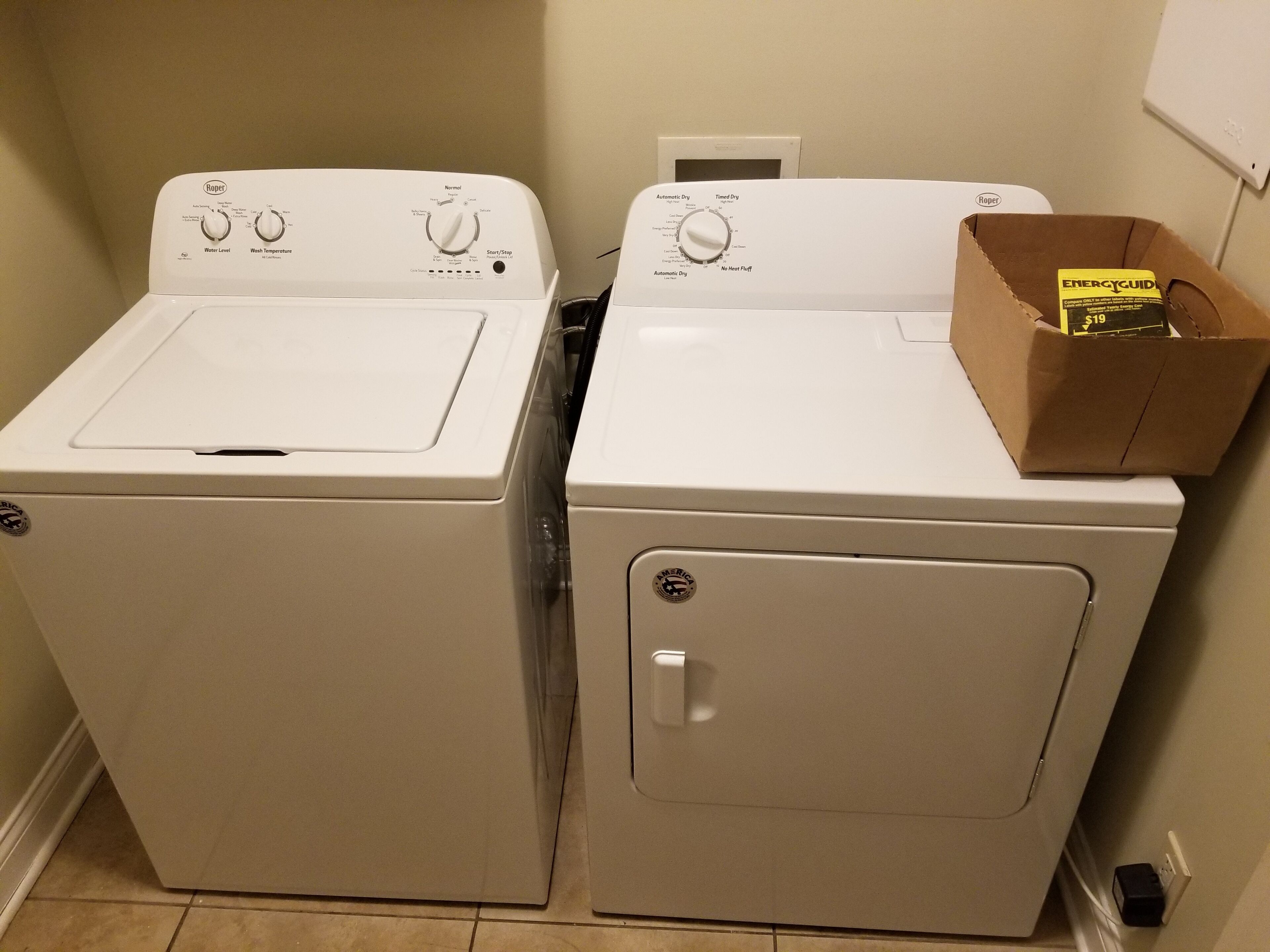 Two front-loading washing machines in a laundry room with a cardboard box on the right.