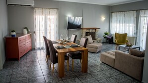 Een woonkamer met een eethoek, een bank, een gele fauteuil, een televisie en een open haard.
