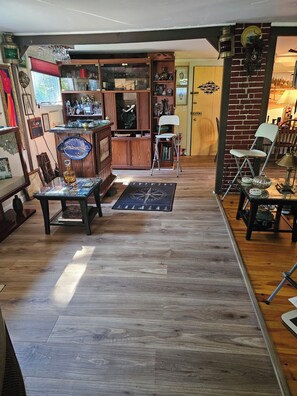 A room with wooden flooring, a compass rug, a white folding chair, and a shelf with various items.