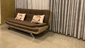 A brown sofa with two pillows, one with a coffee house logo, in front of a window with sheer curtains. - villacork face the river (Galle)