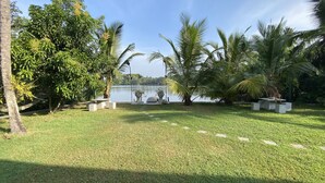 A well-maintained garden with a lawn, palm trees, and a body of water. - villacork face the river (Galle)