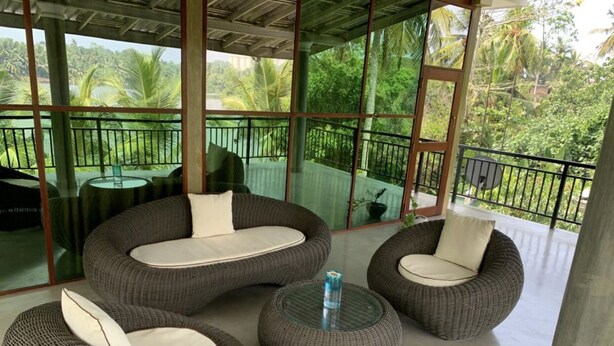 A balcony with wicker furniture, including sofas and a round table, overlooking a lush green landscape. - villacork face the river (Galle)