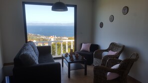A balcony with a view of the sea, a sofa, two wicker chairs, a small table with tea sets, and decorative wall art.