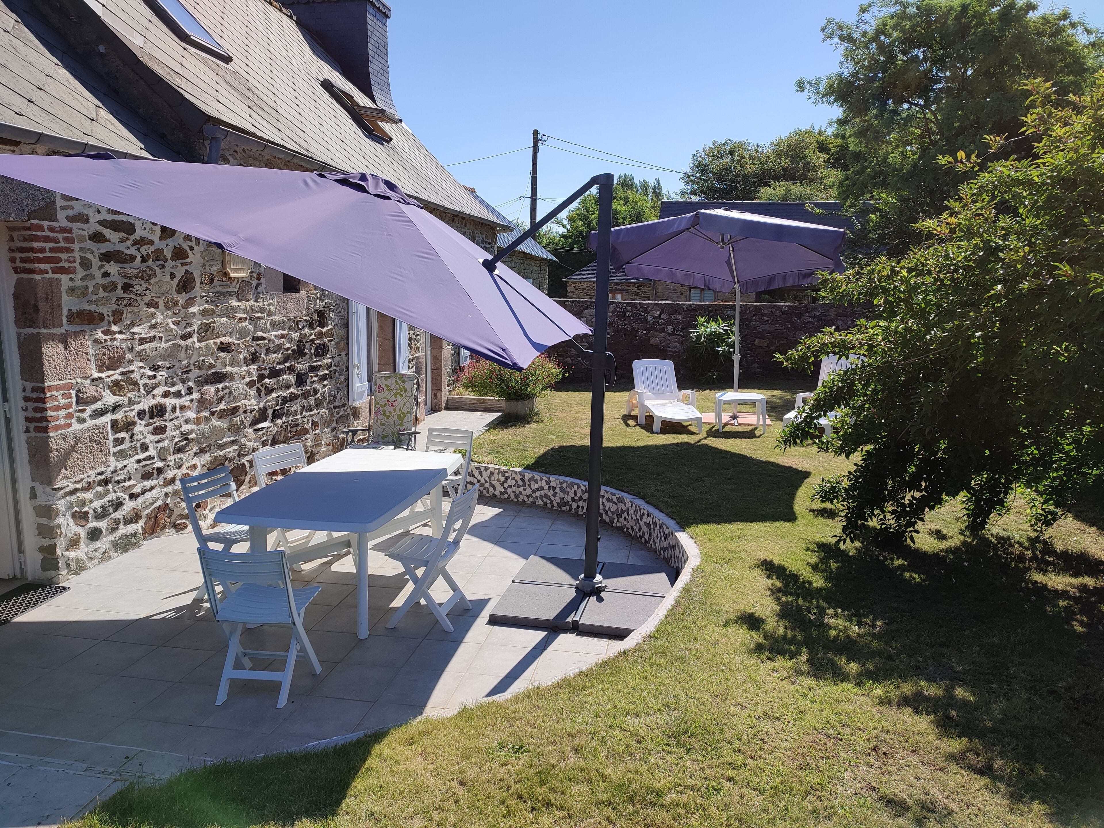 A patio with a stone wall, a table and chairs, and a purple umbrella.