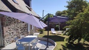 A patio with a stone wall, a table and chairs, and a purple umbrella. - The charm of the Breton countryside (Quemper Guezennec)