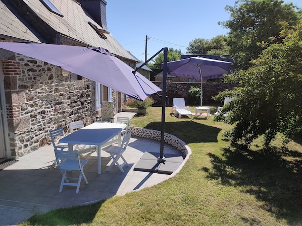 A patio with a stone wall, a table and chairs, and a purple umbrella.