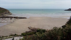 A beach with a parking area filled with boats, a rocky outcrop, and a view of the sea. - The charm of the Breton countryside (Quemper Guezennec)