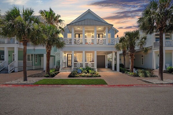 A two-story building with a balcony, palm trees, and a well-maintained lawn. - Designer Cinnamon Shore Lakehouse, Private Fire Pit, Resort-Like Amenities! (Port Aransas)