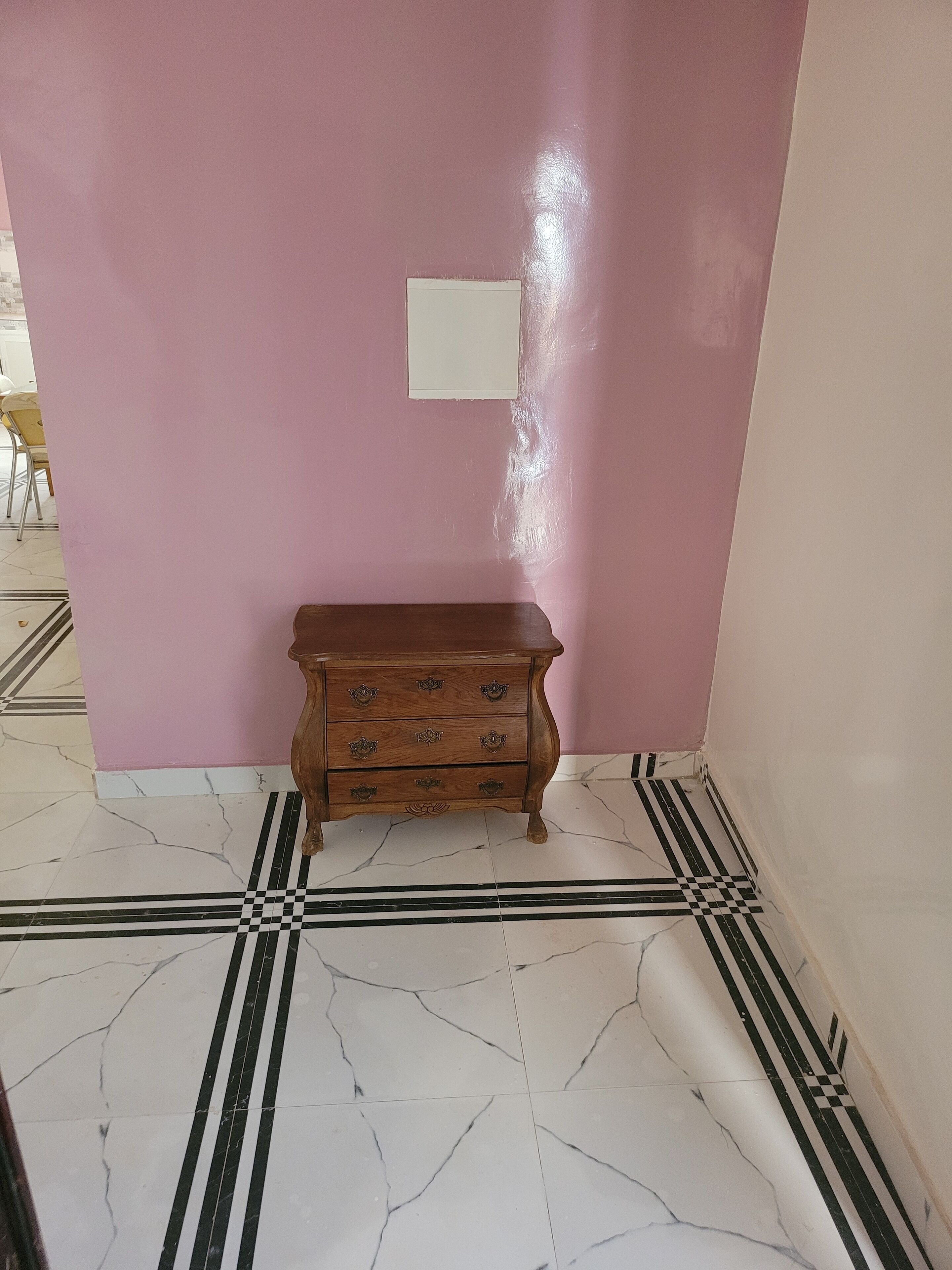 Una habitación con pared rosa, cómoda de madera con cajones y suelo con estampado de cuadros.