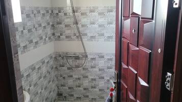 Un baño con baldosas estampadas, ducha, inodoro y puerta de madera.