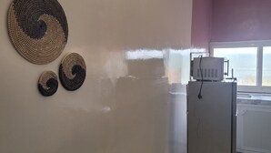 A kitchen with a refrigerator, a window, and decorative woven wall art. - Chez Medzo (Toubab Dialao)