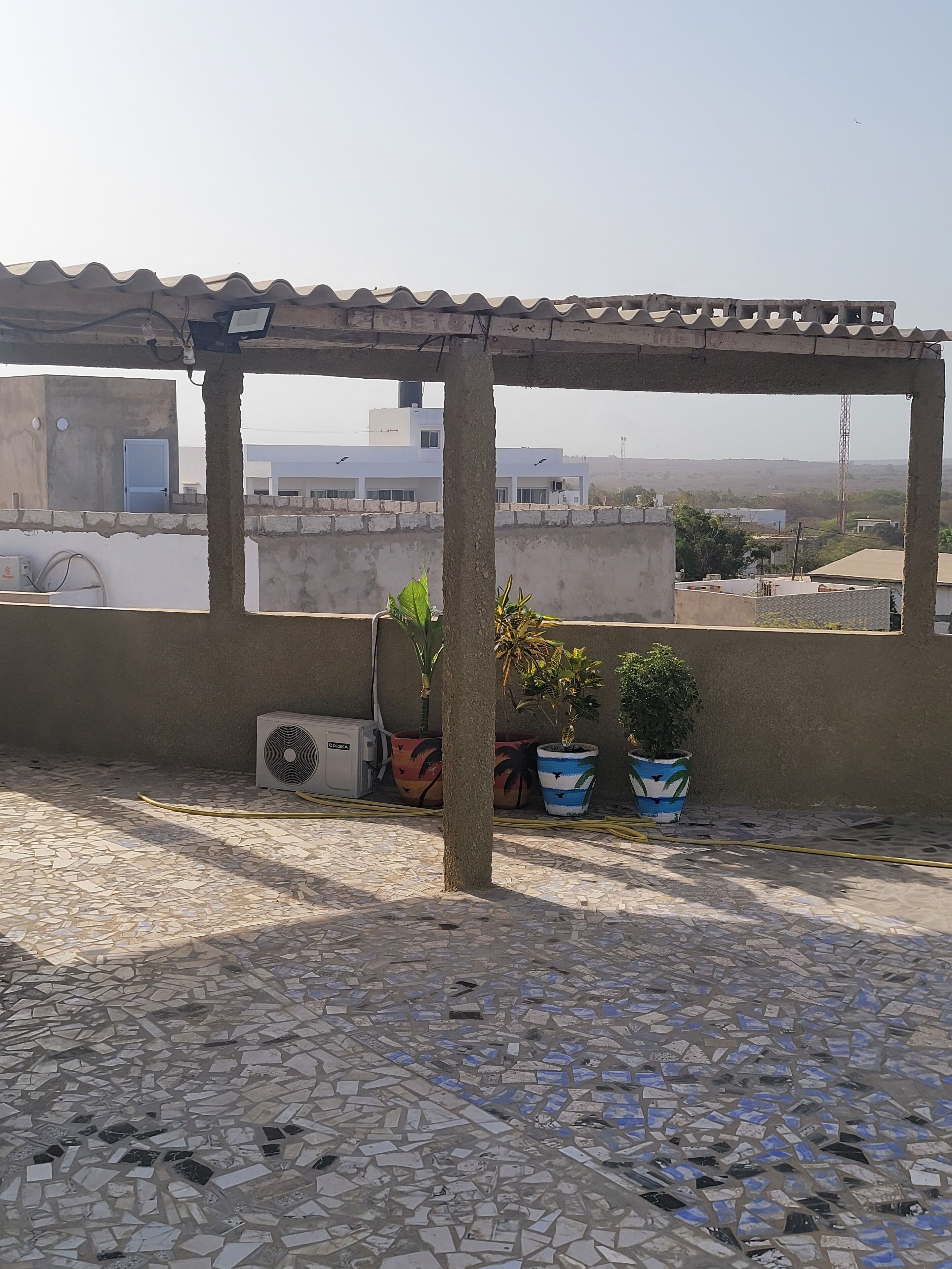 Terraza en la azotea con suelo de baldosas, plantas en macetas y un equipo de aire acondicionado.