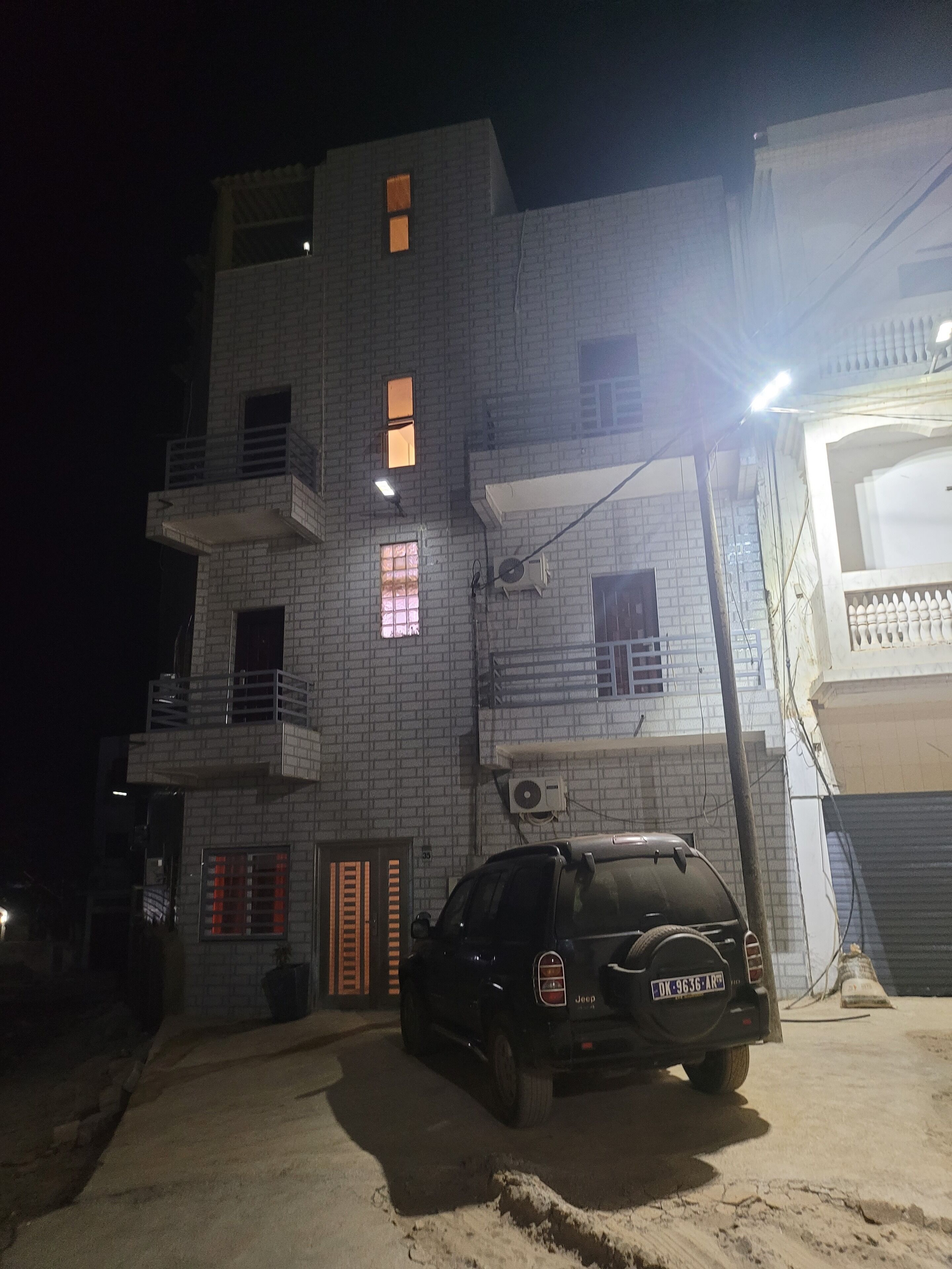 A multi-story building with a brick facade, a Jeep parked in front, and a visible door with a window.